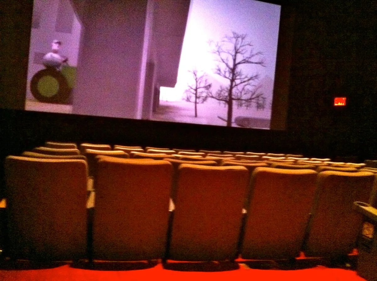 Empty rows of movie theater seats facing a lit screen in a darkened auditorium